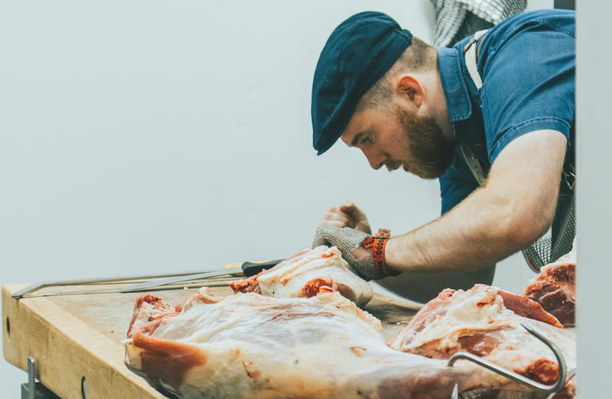 Un apprenti boucher est en train de découper de la viande sur un billot de bois